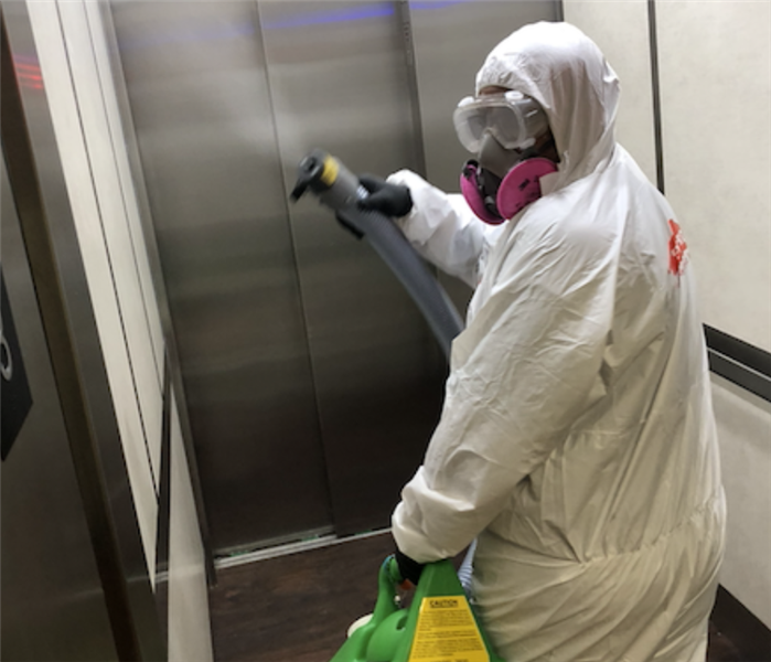 a man with an electrostatic sprayer disinfecting an elevator